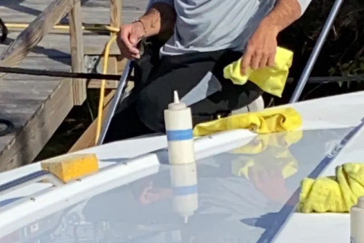 A detailer hand-buffing wax into the foredeck of a boat with a microfiber cloth, working panel by panel