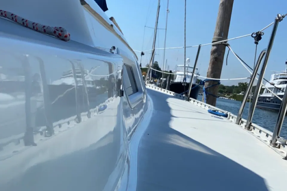 Sunlight raking across the mirror-finished foredeck and stainless bow rail of a freshly waxed yacht at a Long Island marina