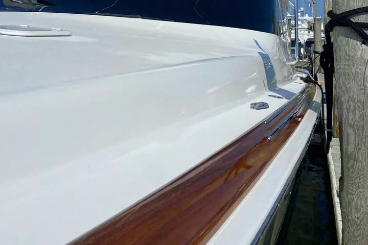 The bow of a white sport fishing boat with a varnished timber toe rail, gelcoat and brightwork both freshly detailed