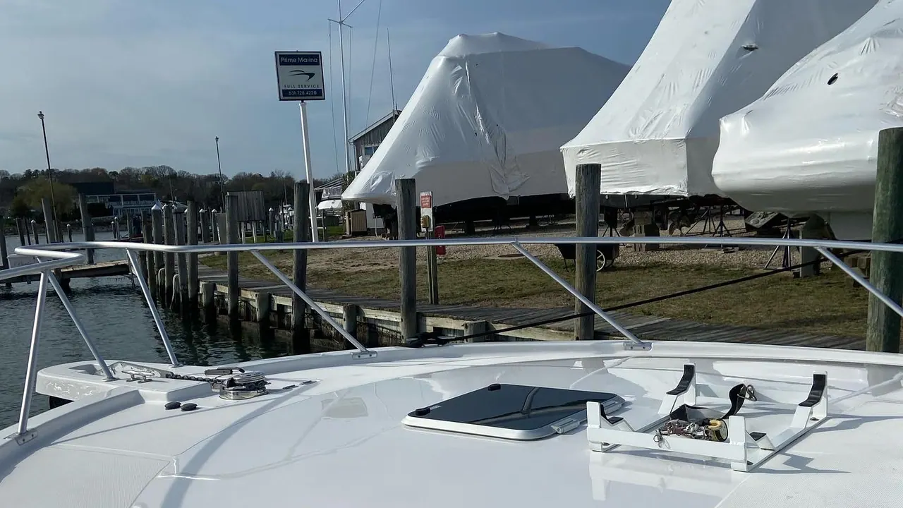 A row of boats sealed under white shrink wrap in the winter storage yard at Prime Marina, seen across the polished foredeck of a boat still in the water