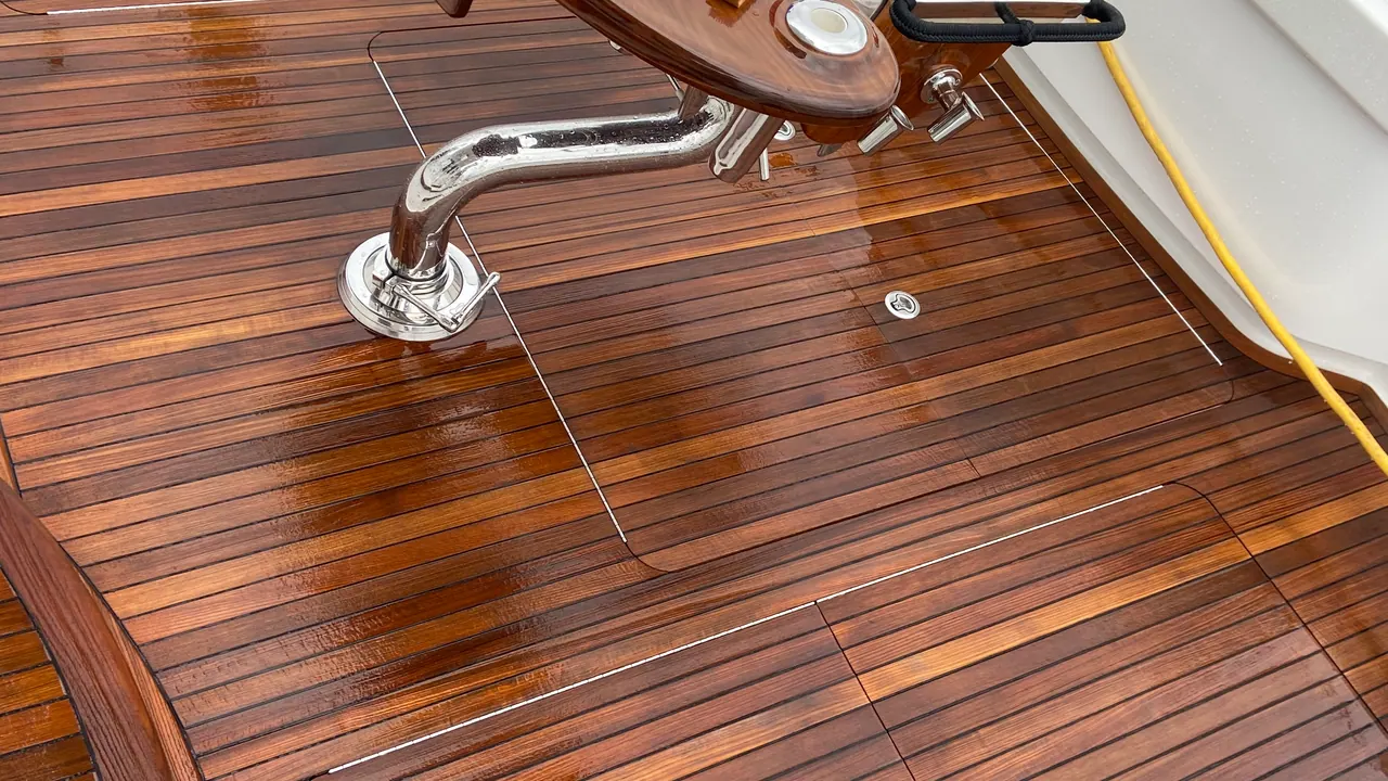A restored teak cockpit deck, freshly cleaned and oiled to a deep honey colour, with scrub brushes, teak cleaner and microfibers set out on the varnished cockpit table