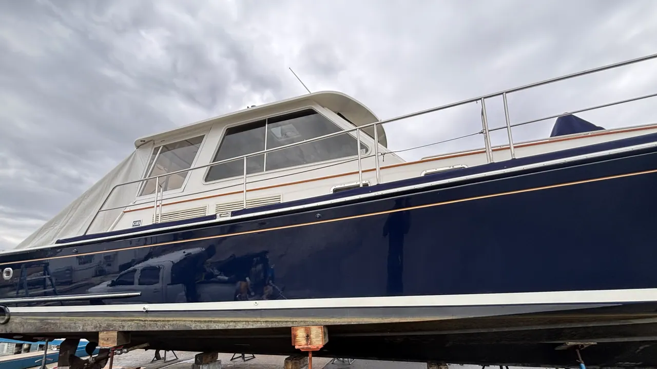 A dark blue motor yacht blocked up on jack stands in an off-season boatyard, hauled out and waiting for its winter layup and spring commissioning